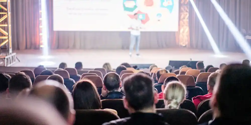 Conference audience watching a speaker on a lit stage