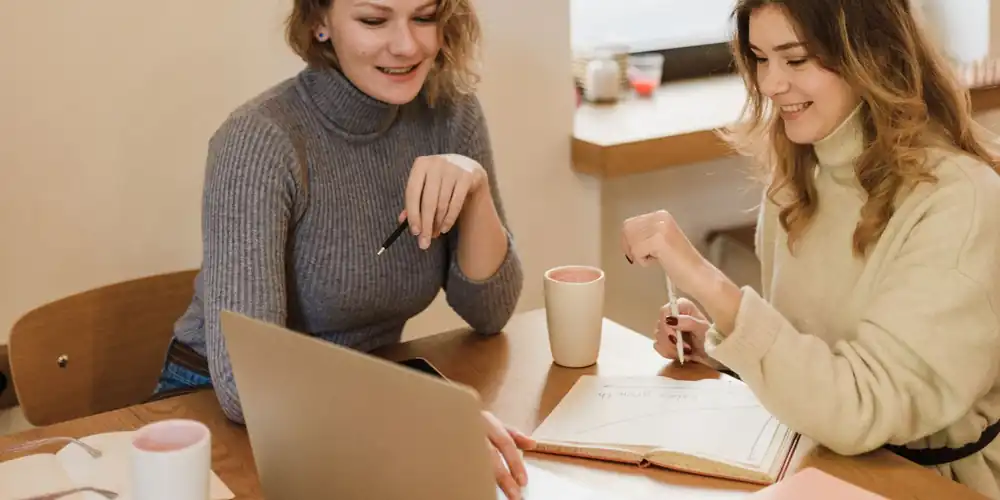Two people sitting at a table working through something together on a laptop